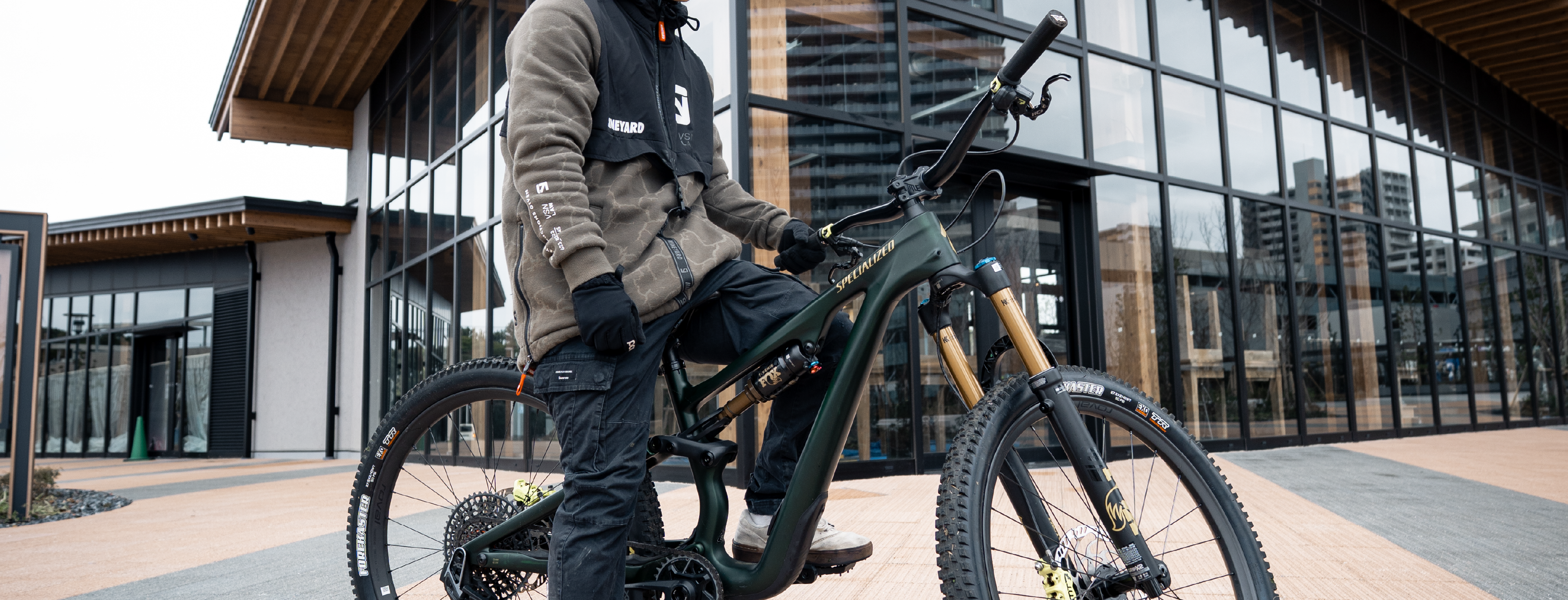 Person holding a mountain bike in an urban setting with modern buildings in the background