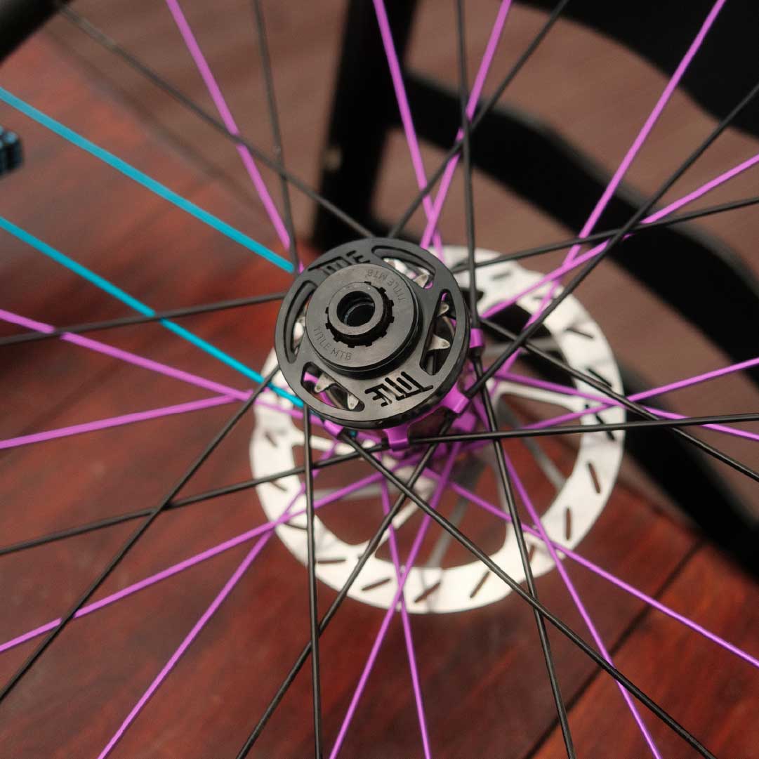 Close-up of a bicycle wheel with pink and black spokes on a wooden floor.